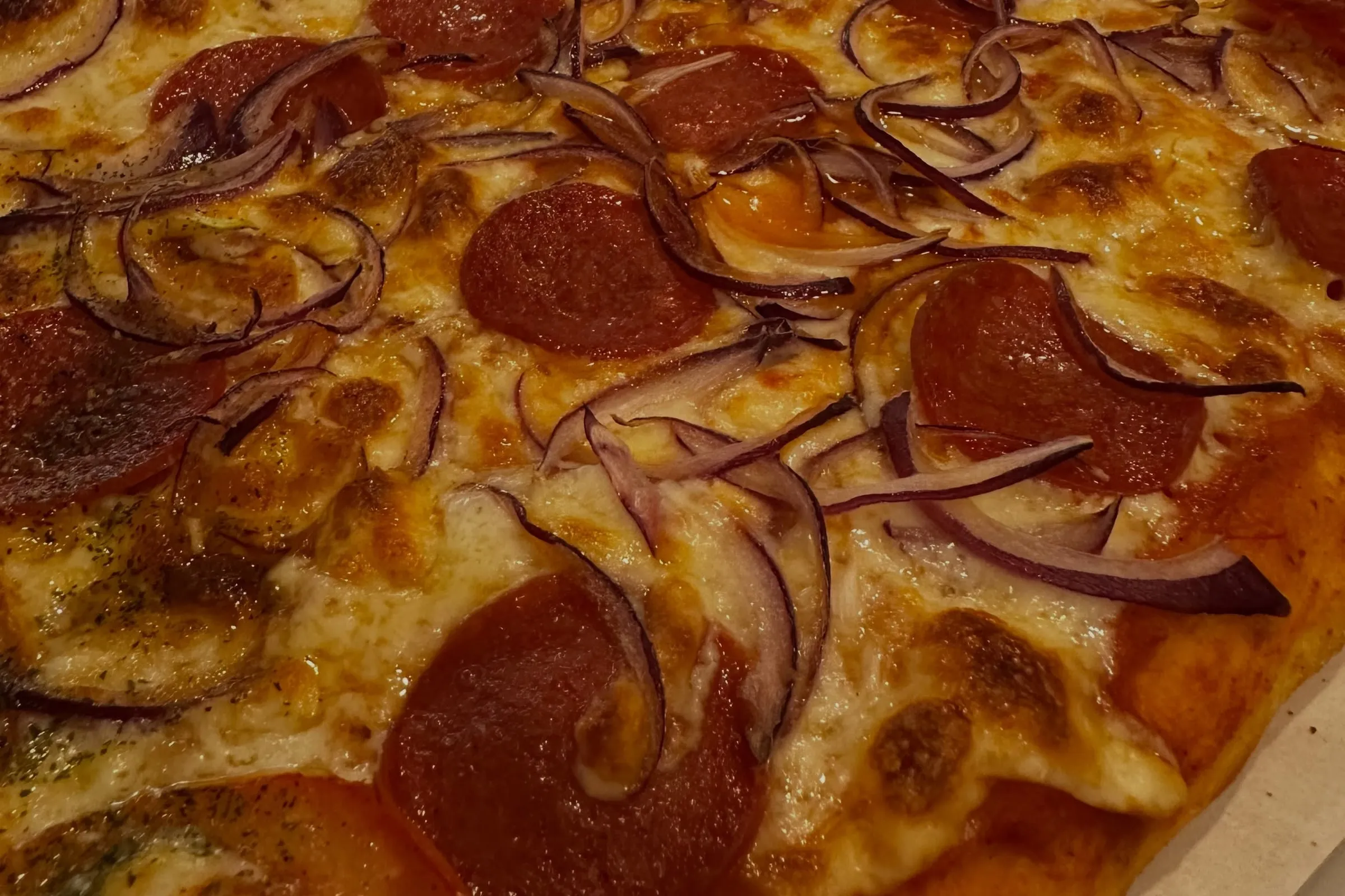 A ponta de pepperoni da pizza ao metro, com cebola roxa sobre a mozzarella.
